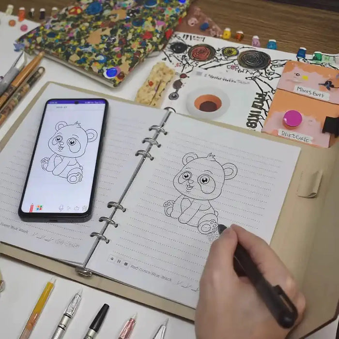 Hand drawing a cute cartoon panda in a notebook, referencing a digital sketch on a smartphone, with art supplies nearby TUTT