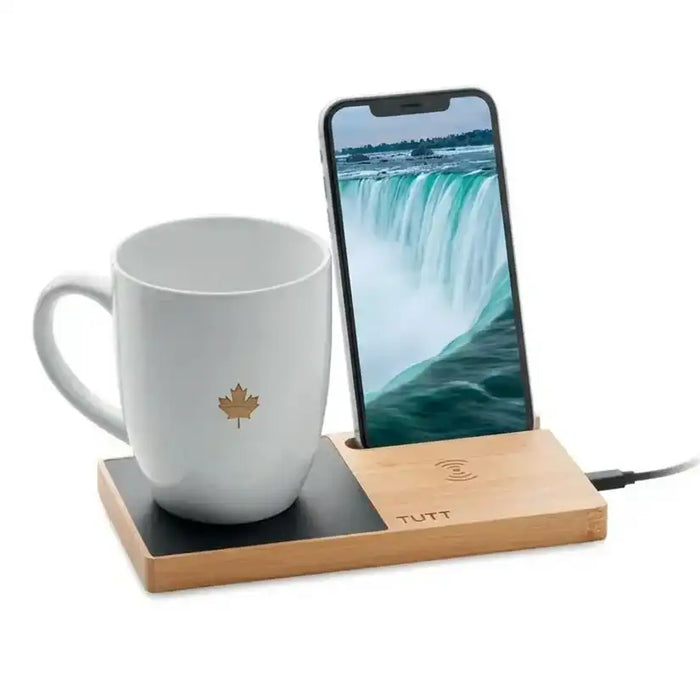 White mug with a maple leaf design on a wooden charging station with a smartphone displaying a waterfall. TUTT 15W Wireless Charger – Bamboo Cup Warmer & Phone Stand