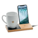 White mug with a maple leaf design on a wooden charging station with a smartphone displaying a waterfall. TUTT 15W Wireless Charger – Bamboo Cup Warmer & Phone Stand