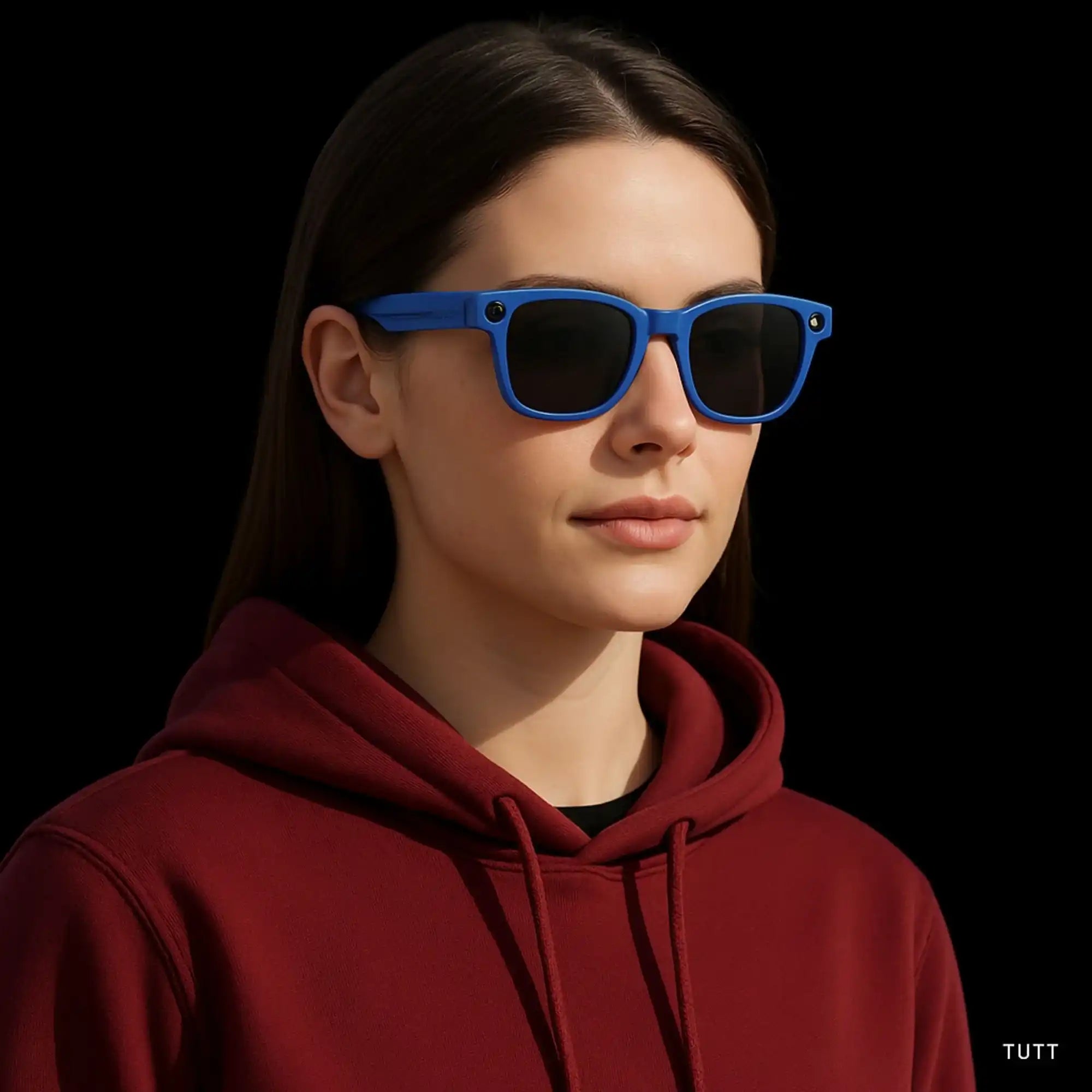 Woman wearing blue smart camera sunglasses with black lenses and maroon hoodie against black background TUTT