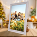 Digital photo frame displaying a smiling family of five in a vibrant outdoor flower field, modern white frame TUTT