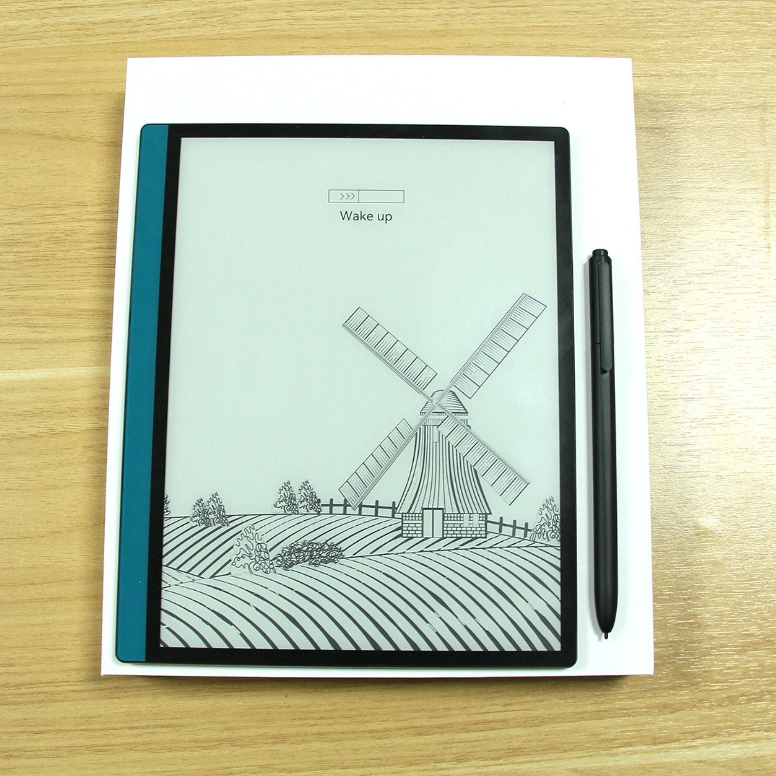 E-reader with black stylus pen on wooden table displaying windmill sketch and wake up loading bar TUTT
