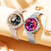 Two TUTT NX17 Pro smart watches for women with mesh straps on a beige surface, one showing a floral artistic face and the other with a colorful gem-like digital face, both surrounded by decorative jewelry. TUTT